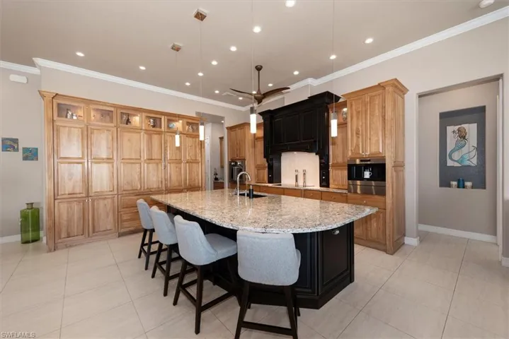 Kitchen featuring a breakfast bar, decorative backsplash, a large island with sink, light stone counters, and light tile patterned floors