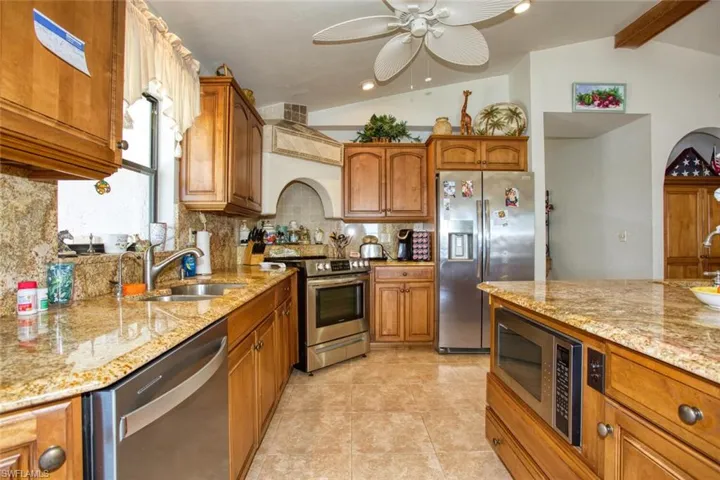 Kitchen featuring stainless steel appliances, vaulted ceiling with beams, brown cabinetry, and a sink
