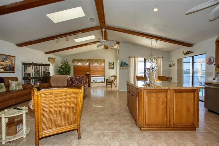 Kitchen with brown cabinetry, plenty of natural light, lofted ceiling with skylight, and ceiling fan with notable chandelier