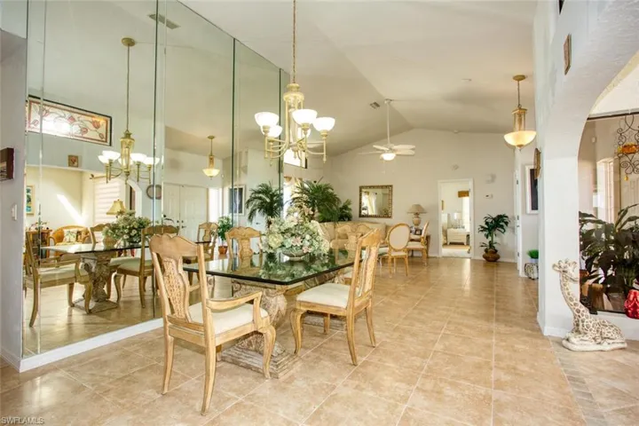 Dining space featuring light tile patterned floors, high vaulted ceiling, arched walkways, ceiling fan with notable chandelier, and baseboards