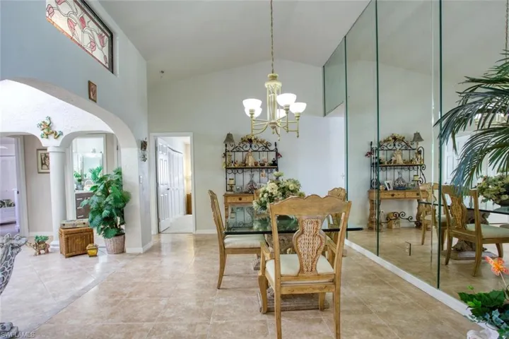 Dining area with arched walkways, high vaulted ceiling, light tile patterned flooring, baseboards, and an inviting chandelier