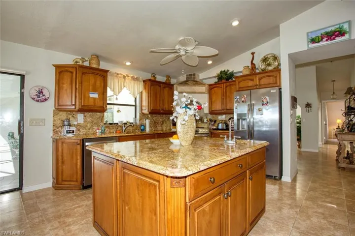 Kitchen with stainless steel appliances, brown cabinetry, light stone counters, and tasteful backsplash