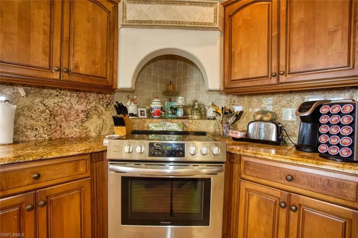 Kitchen with brown cabinetry, stainless steel electric range, light stone countertops, and decorative backsplash