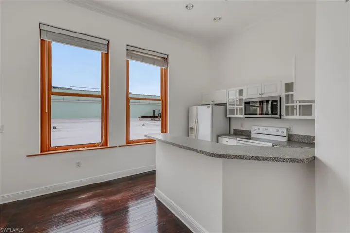Kitchen with dark hardwood / wood-style floors, kitchen peninsula, crown molding, white cabinets, and white appliances