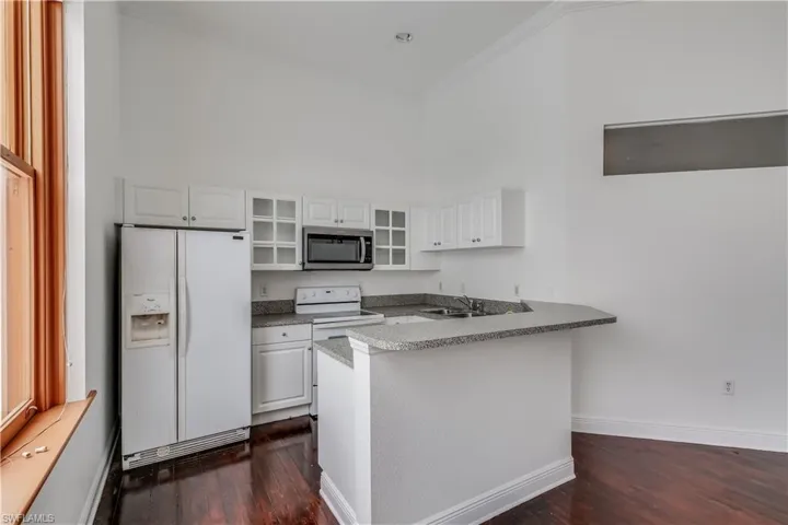 Kitchen with white appliances, dark hardwood / wood-style floors, and white cabinetry