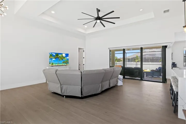 Living area with a tray ceiling, a ceiling fan, wood finished floors, recessed lighting, and a high ceiling