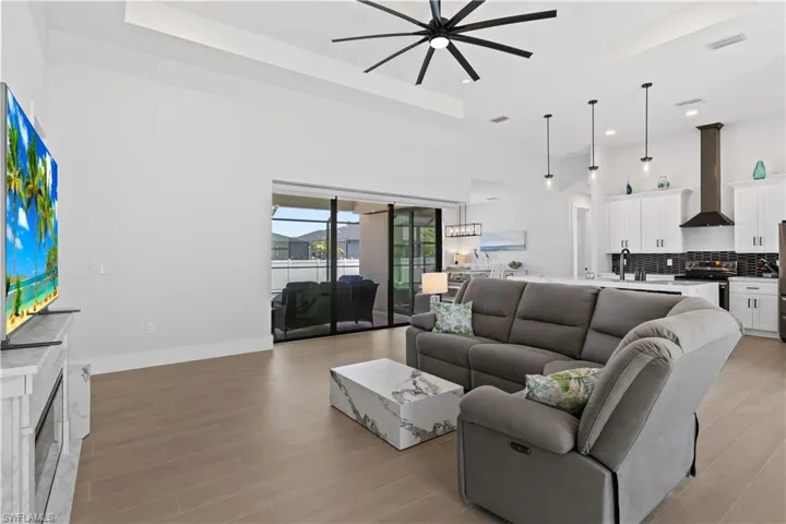 Living area featuring ceiling fan, a raised ceiling, light wood-type flooring, recessed lighting, and a towering ceiling