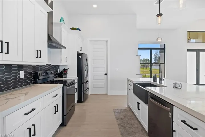 Kitchen with appliances with stainless steel finishes, wall chimney range hood, backsplash, white cabinetry, and decorative light fixtures