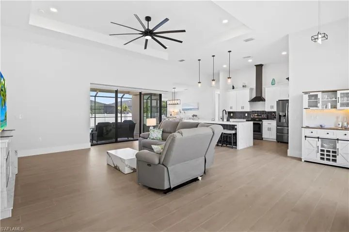 Living area featuring a tray ceiling, a towering ceiling, recessed lighting, ceiling fan, and light wood-type flooring