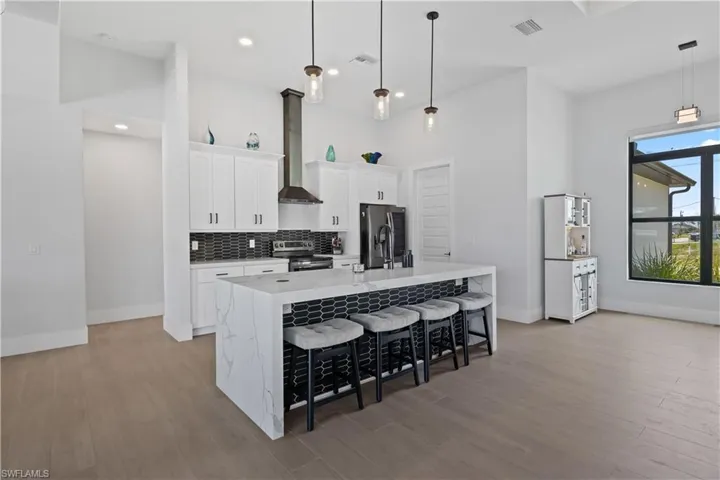 Kitchen featuring stainless steel appliances, wall chimney range hood, a kitchen island with sink, light wood finished floors, and recessed lighting