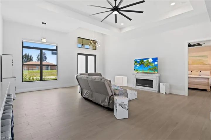 Living area featuring a raised ceiling, a fireplace, wood finished floors, recessed lighting, and a chandelier