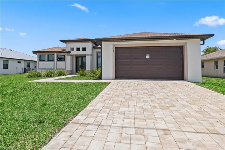 Prairie-style home featuring decorative driveway, a front lawn, an attached garage, and stucco siding
