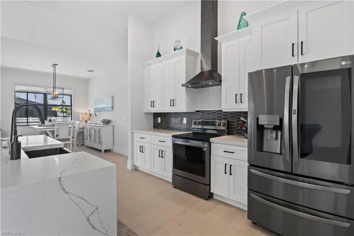 Kitchen featuring appliances with stainless steel finishes, wall chimney range hood, white cabinetry, decorative backsplash, and light wood-style floors