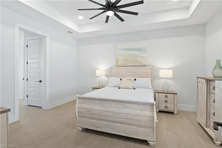 Bedroom with a raised ceiling, light wood-type flooring, recessed lighting, and a ceiling fan