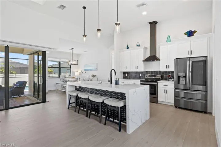 Kitchen with appliances with stainless steel finishes, wall chimney range hood, a kitchen breakfast bar, light wood-type flooring, and decorative backsplash