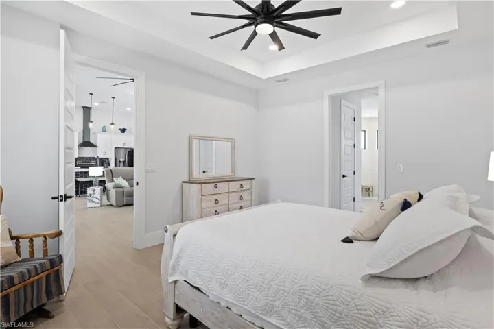 Bedroom with stainless steel fridge, recessed lighting, light wood-type flooring, a tray ceiling, and connected bathroom