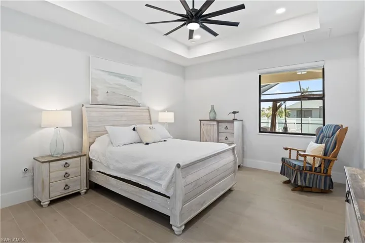 Bedroom featuring a raised ceiling, light wood finished floors, recessed lighting, and a ceiling fan