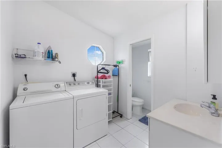 Clothes washing area with washer and clothes dryer, light tile patterned flooring, and sink