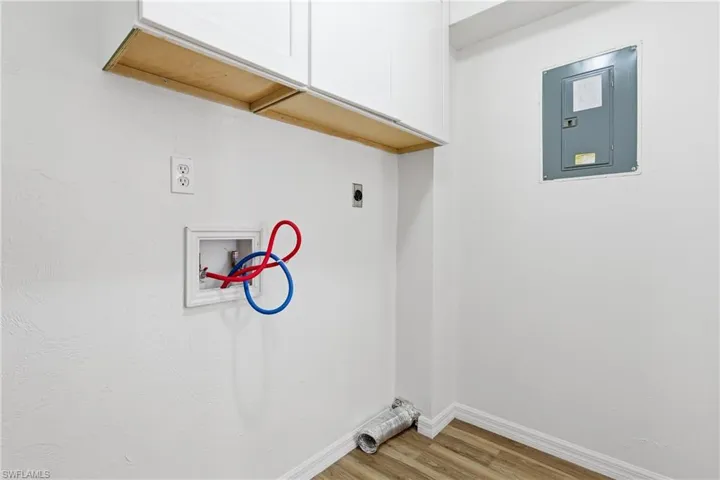 Laundry area with light wood-type flooring, electric panel, hookup for a washing machine, cabinet space, and hookup for an electric dryer