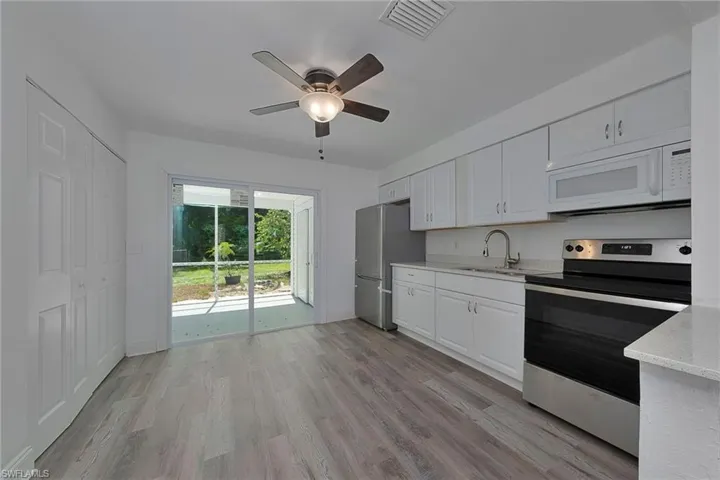 Kitchen with appliances with stainless steel finishes, light hardwood / wood-style flooring, light stone countertops, white cabinetry, and ceiling fan