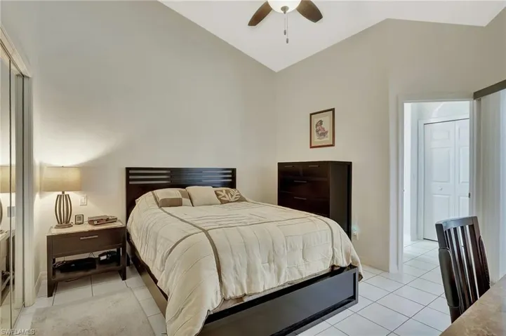Vaulted ceiling bedroom featuring white tile flooring, a mirrored sliding closet, and a ceiling fan