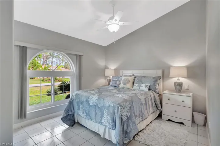 Bedroom featuring an arched window, white tile flooring, a sloped ceiling, and a ceiling fan with integrated lighting