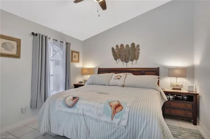Vaulted ceiling bedroom featuring light-toned tile flooring, a window with an arched transom, and a ceiling fan with integrated lighting