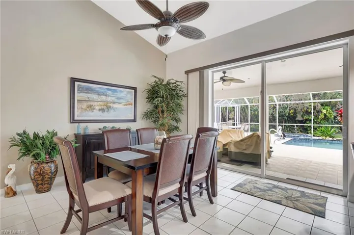 Vaulted ceiling dining area featuring tile flooring and sliding glass doors opening to a screened patio with a swimming pool