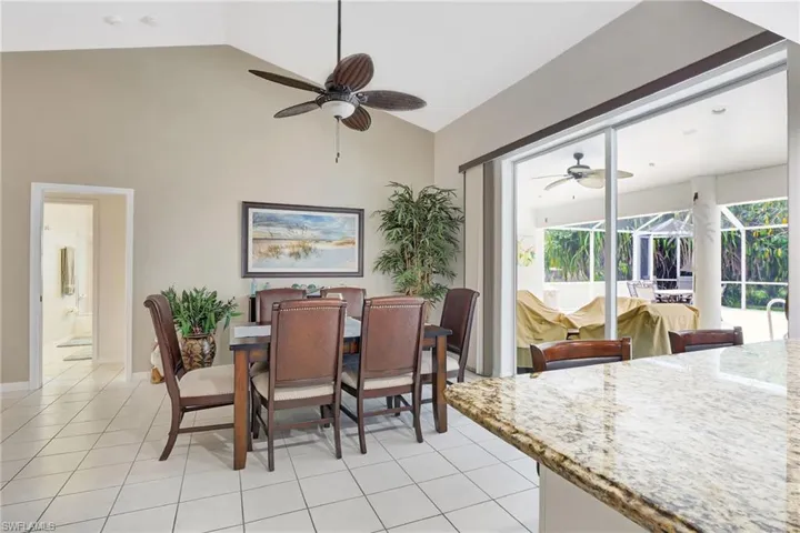 Dining area featuring vaulted ceilings, light-toned tile flooring, and a ceiling fan with integrated lighting