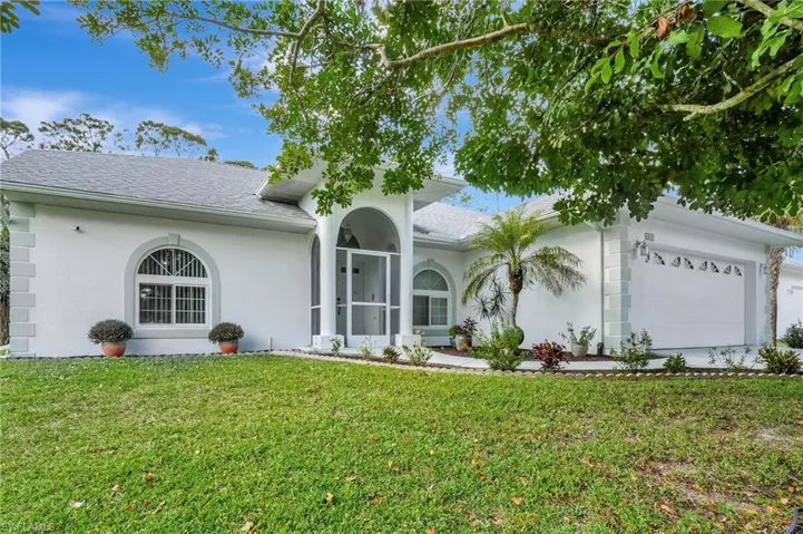 Stucco exterior with arched windows, screened entryway, attached garage, and mature landscaping