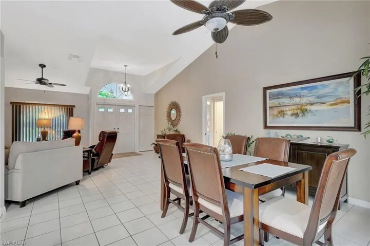 Expansive living area featuring vaulted ceilings, tile flooring throughout, a double entry door with an arched transom, and a ceiling fan with integrated lighting