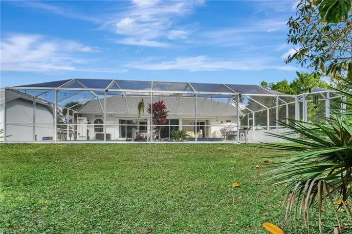 Rear exterior with a screened enclosure, a patio area, and a lush green lawn