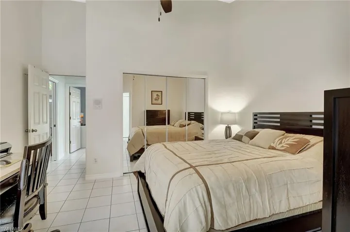 Bedroom featuring high vaulted ceilings, white tile flooring, mirrored closet doors, and solid panel interior doors