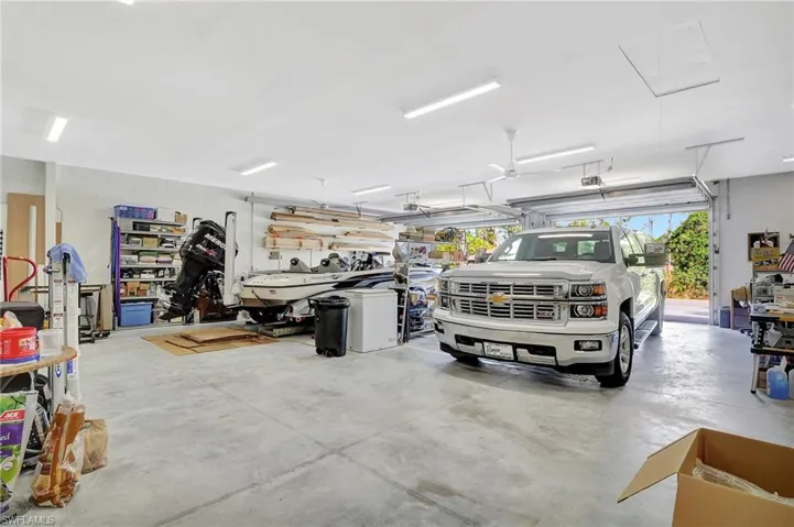 Spacious garage featuring a concrete floor, multiple fluorescent light fixtures, ceiling fan, and two overhead garage doors