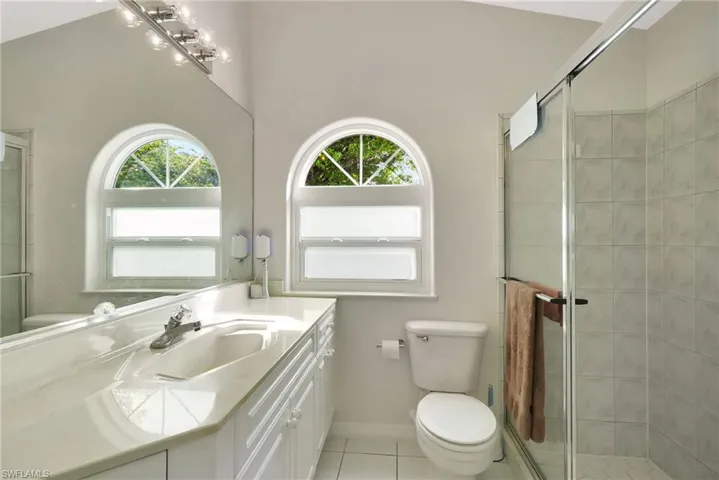 Bathroom featuring a white vanity with an integrated sink, a large wall-mounted mirror, and an arched window