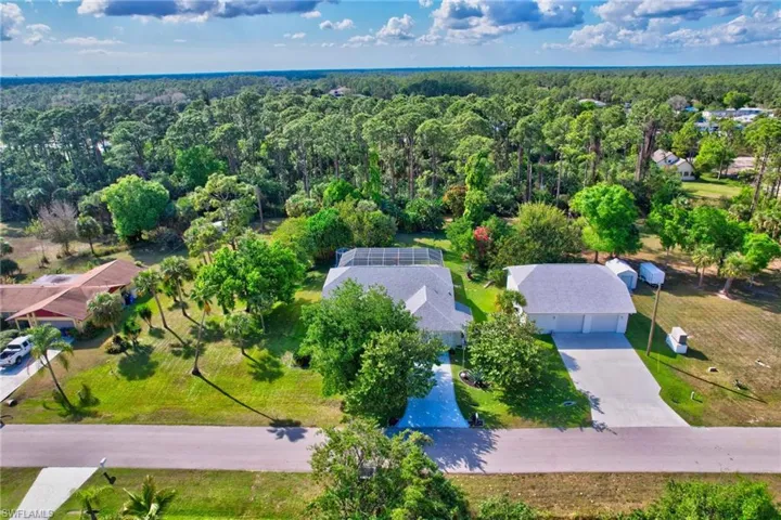 Aerial view showcasing a residential property with a main house, detached garage, and a screened enclosure