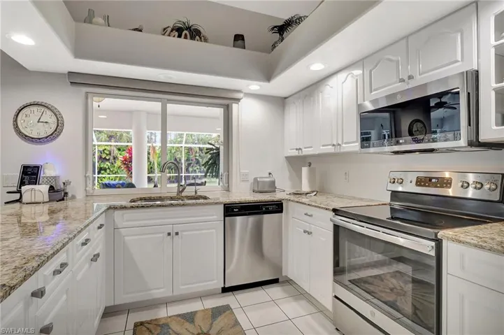 Kitchen featuring light-toned countertops, white cabinetry with silver-tone hardware, stainless steel appliances, and a large window above the sink