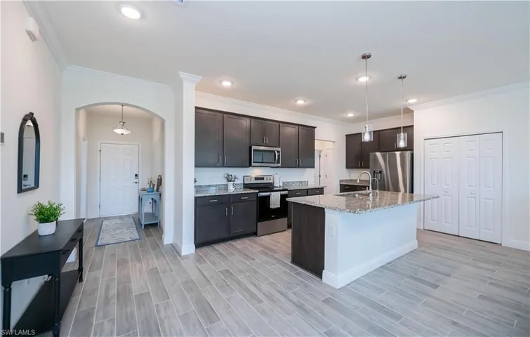 Kitchen with appliances with stainless steel finishes, pendant lighting, light stone countertops, ornamental molding, and dark brown cabinets