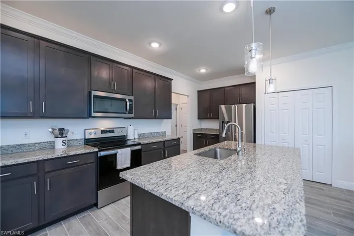 Kitchen with wood tiled floors, appliances with stainless steel finishes, light stone counters, ornamental molding, and pendant lighting