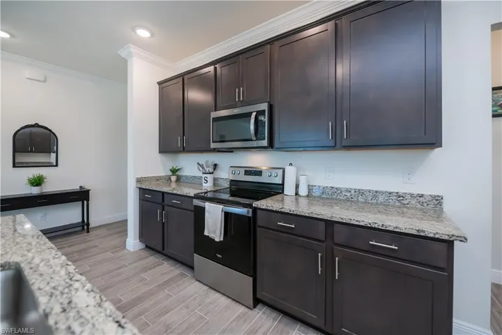 Kitchen featuring appliances with stainless steel finishes, ornamental molding, light stone counters, wood finish floors, and dark brown cabinetry