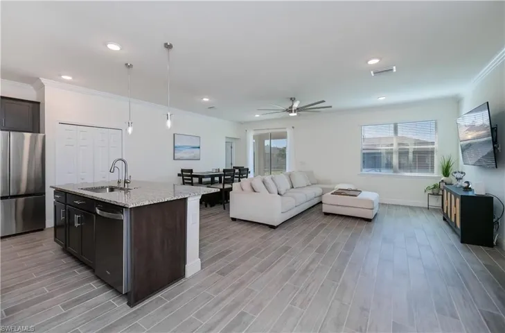 Kitchen with stainless steel appliances, light stone countertops, open floor plan, decorative light fixtures, and crown molding