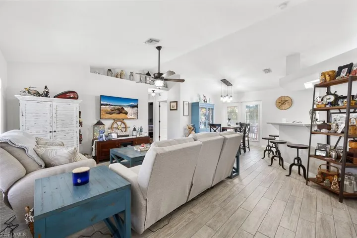Living area featuring vaulted ceiling, light plank-style flooring, and ceiling fan