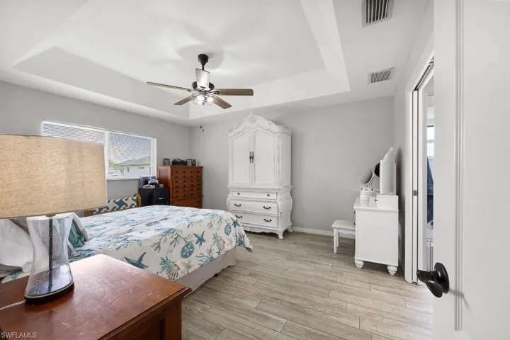 Bedroom with a raised ceiling, wood finished floors, and ceiling fan