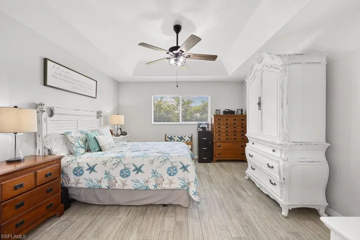 Bedroom with a tray ceiling, light wood-type flooring, and a ceiling fan