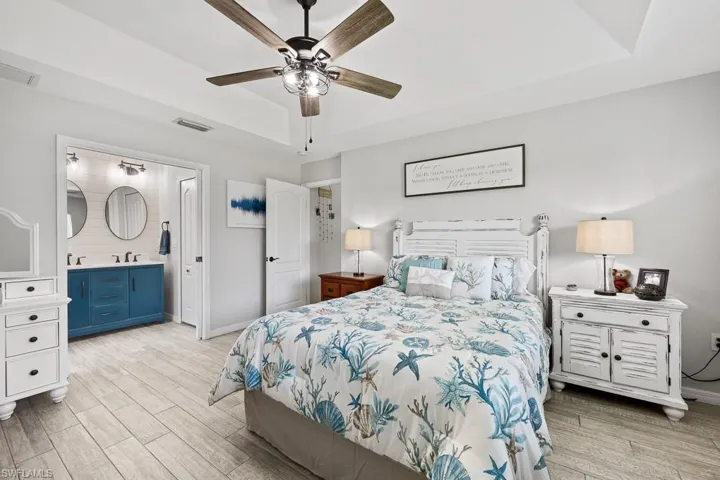 Bedroom featuring a raised ceiling, light wood-style flooring, ceiling fan, and ensuite bath