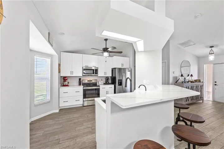 Kitchen featuring appliances with stainless steel finishes, white cabinetry, a kitchen bar, light wood-style floors, and lofted ceiling