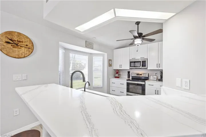 Kitchen with appliances with stainless steel finishes, white cabinets, a peninsula, light stone countertops, and a breakfast bar area
