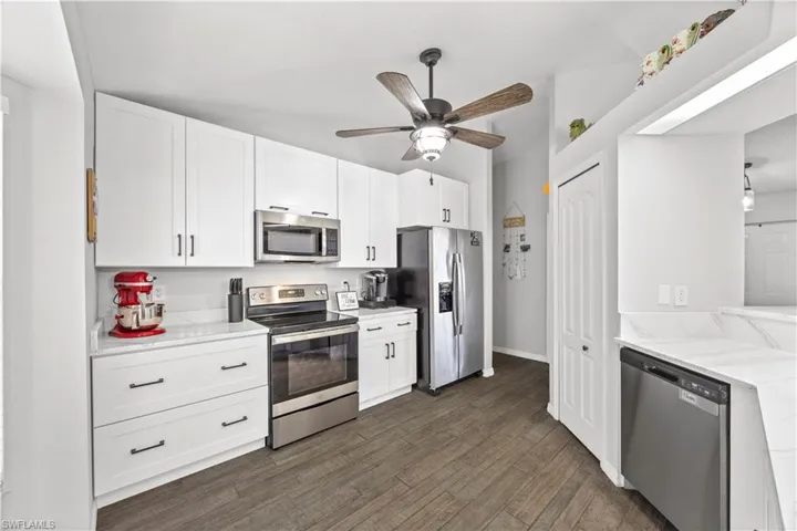 Kitchen with appliances with stainless steel finishes, white cabinets, dark wood-type flooring, and light stone counters