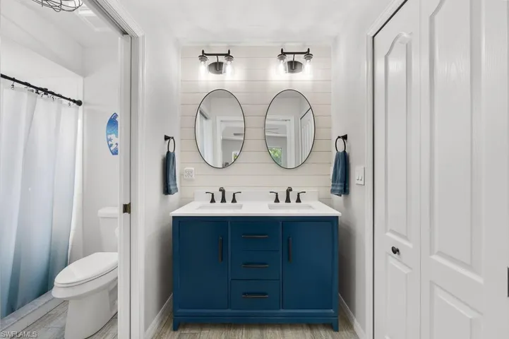 Full bathroom featuring double vanity, light wood finished floors, a closet, a shower with curtain, and wooden walls