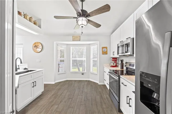 Kitchen with stainless steel appliances, white cabinetry, light wood-style flooring, and ceiling fan